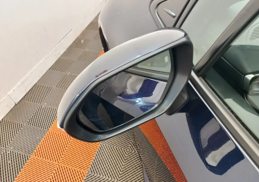 Rétroviseur côté gauche d'une Toyota Corolla hybride bleu, avec partie de la portière visible en intérieur lumineux.