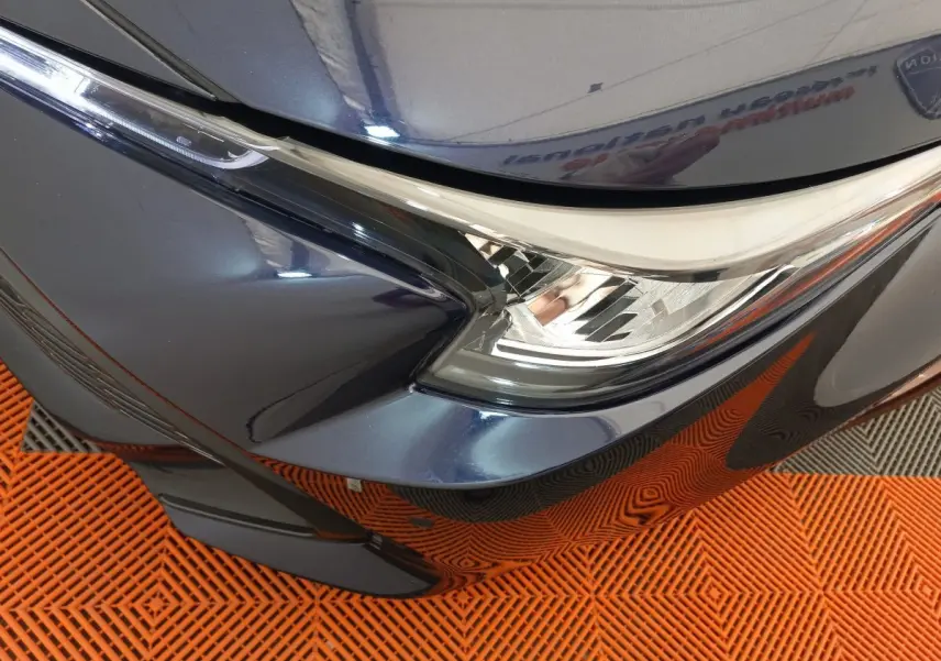 Gros plan sur le phare avant droit bleu métallisé de la Toyota Corolla Hybride 2022 avec détails du pare-chocs et calandre.