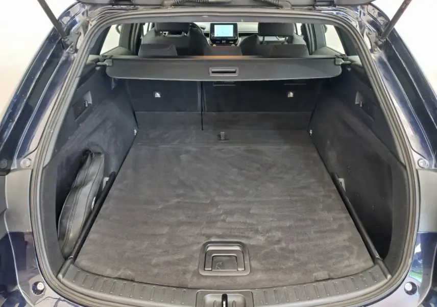 Coffre ouvert vu de l'arrière d'une Toyota Corolla hybride bleu, avec banquette arrière et écran tactile visibles.