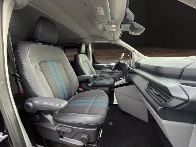 Vue intérieure côté conducteur du Ford Transit Fourgon 2026, sièges tissu gris avec bandes bleues et tableau de bord moderne.