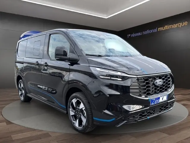Vue 3/4 avant du Ford Transit Fourgon noir avec détails bleus et calandre hexagonale dans un showroom.