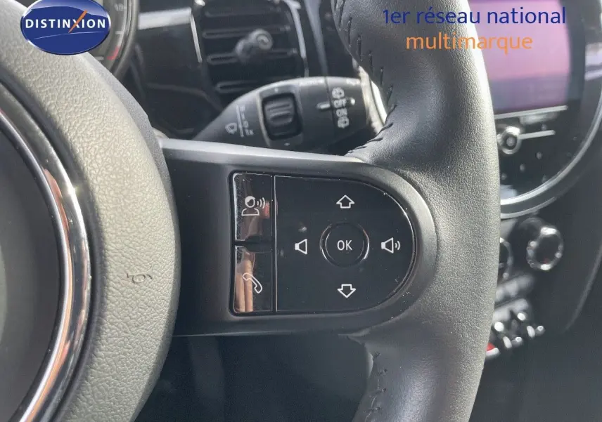 Gros plan sur les commandes multifonctions du volant en cuir noir d'une MINI 2023, avec tableau de bord flou en arrière-plan.