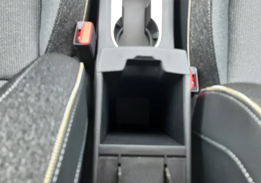Vue plongeante sur la console centrale noire avec porte-gobelets et accoudoirs en tissu gris à surpiqûres jaunes.