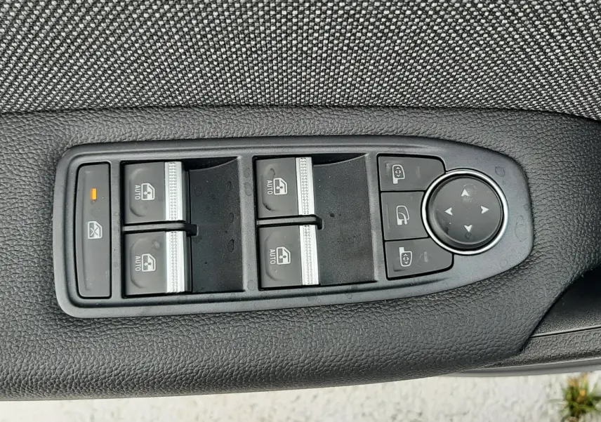 Gros plan sur les commandes de lève-vitres et rétroviseurs sur la porte intérieure noire du Renault Symbioz blanc nacré.