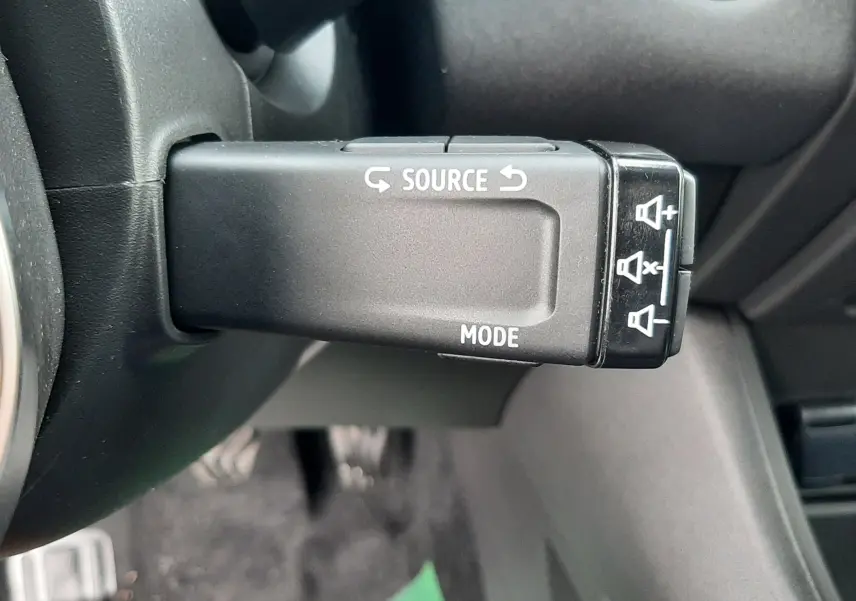 Gros plan sur la commande au volant du Renault Symbioz blanc nacré, montrant les boutons source et mode.