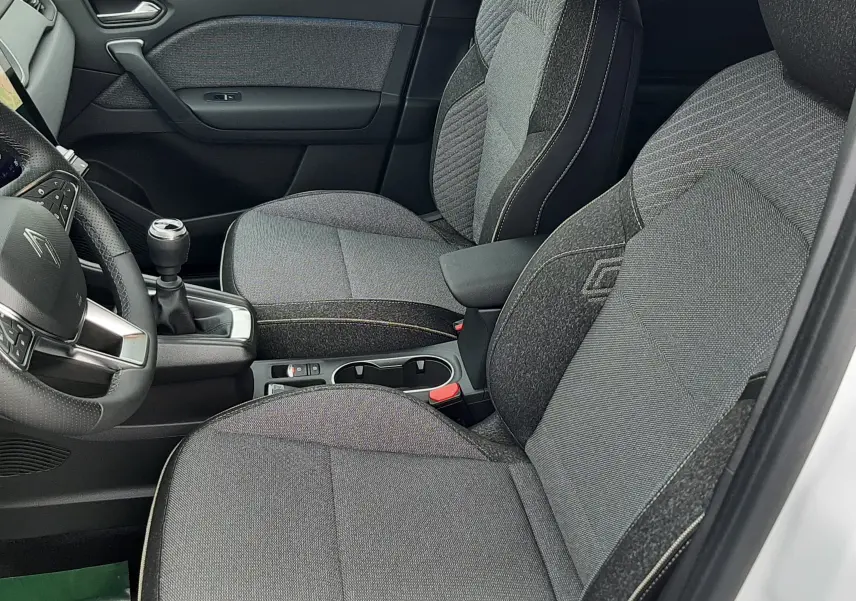 Vue intérieure côté conducteur de la Renault Symbioz blanc nacré, sièges tissu gris avec surpiqûres claires et volant multifonction.