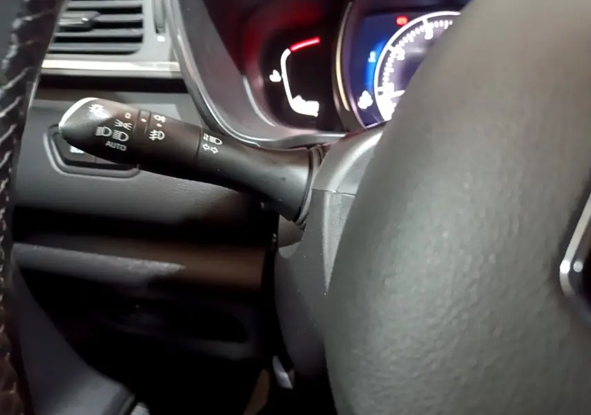 Gros plan sur la manette de commande des phares et clignotants à gauche du volant d’un Renault Kadjar noir, tableau de bord éclairé.