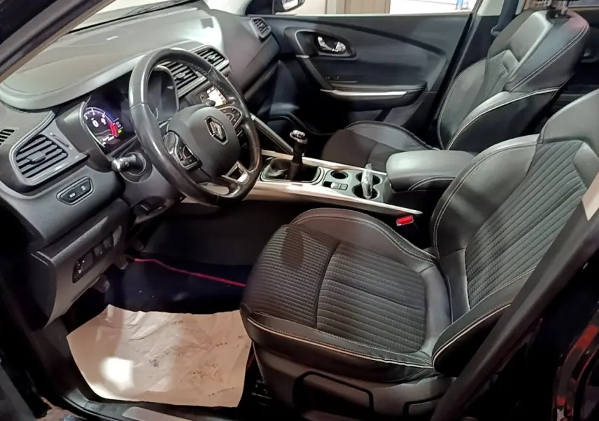 Intérieur avant du Renault Kadjar Intens noir, vue côté conducteur montrant volant cuir, sièges tissu et console centrale avec boîte manuelle.