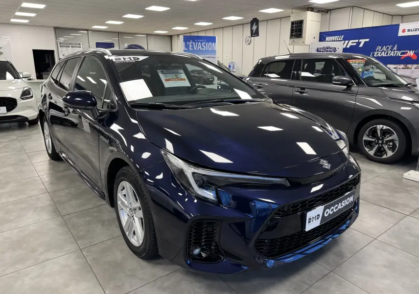 Vue 3/4 avant d'une Suzuki Swace hybride bleu foncé en showroom, avec calandre noire et jantes argentées.