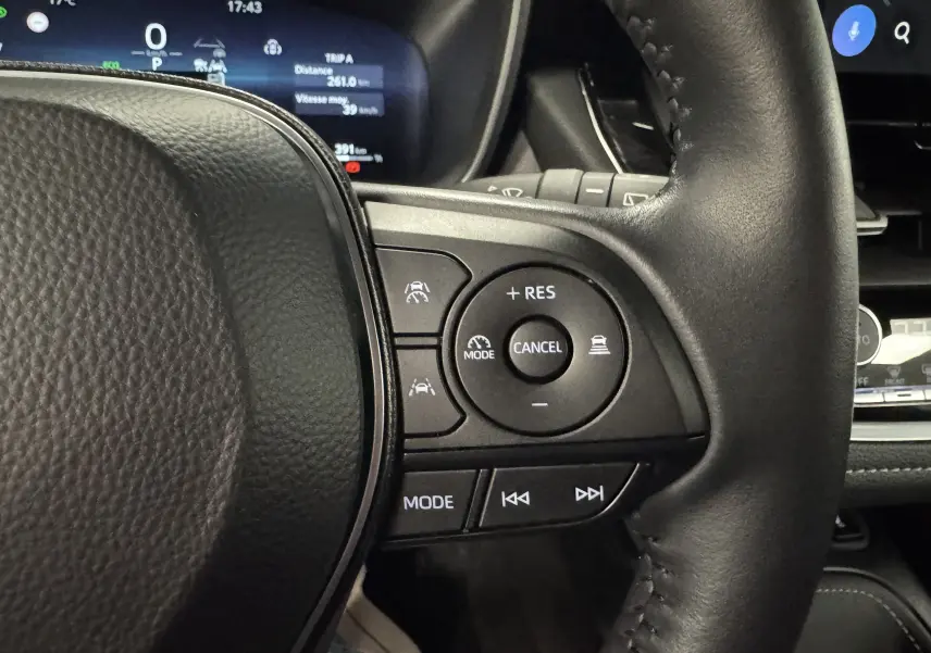 Gros plan sur le volant noir du Suzuki Swace 1.8 140CH Pack Full Hybrid 2025, avec commandes de régulateur et écran digital en arrière-plan.