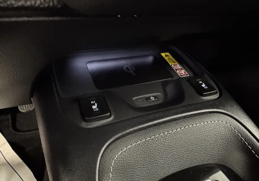 Gros plan sur la console centrale noire avec commandes de sièges chauffants et chargeur sans fil dans Suzuki Swace bleu 2025.