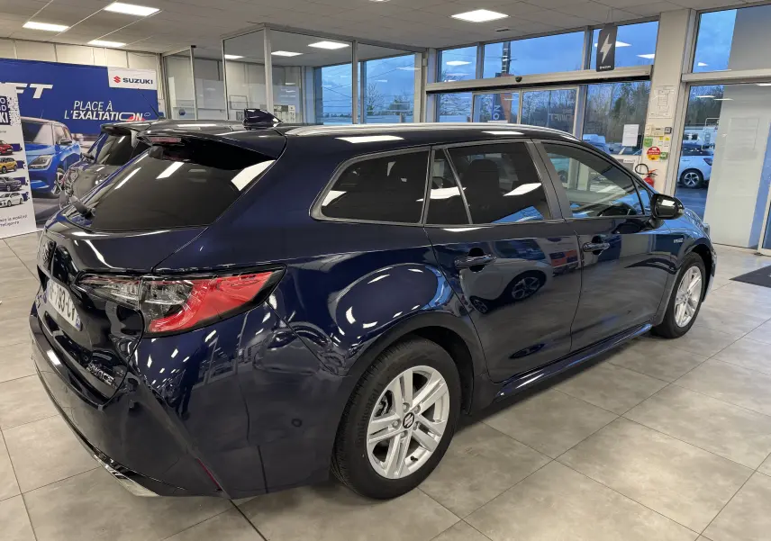 Vue 3/4 arrière droite d'une Suzuki Swace bleu foncé hybride, en showroom avec vitres teintées et jantes argentées.