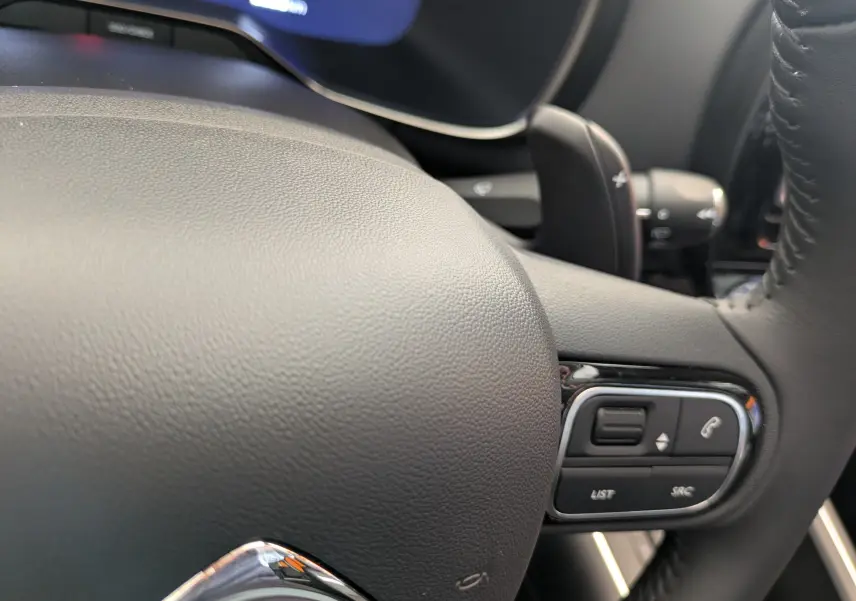 Gros plan sur le volant en cuir gris du Citroën C5 Aircross hybride 2025, avec commandes intégrées et palettes au volant.