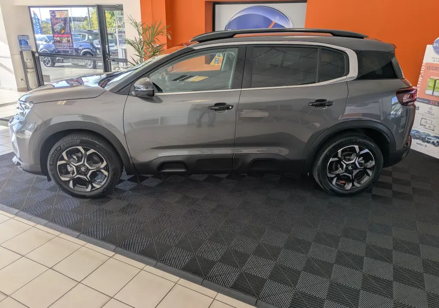 Vue de profil côté gauche d'un Citroën C5 Aircross hybride gris platinium avec jantes biton 18 pouces en showroom.