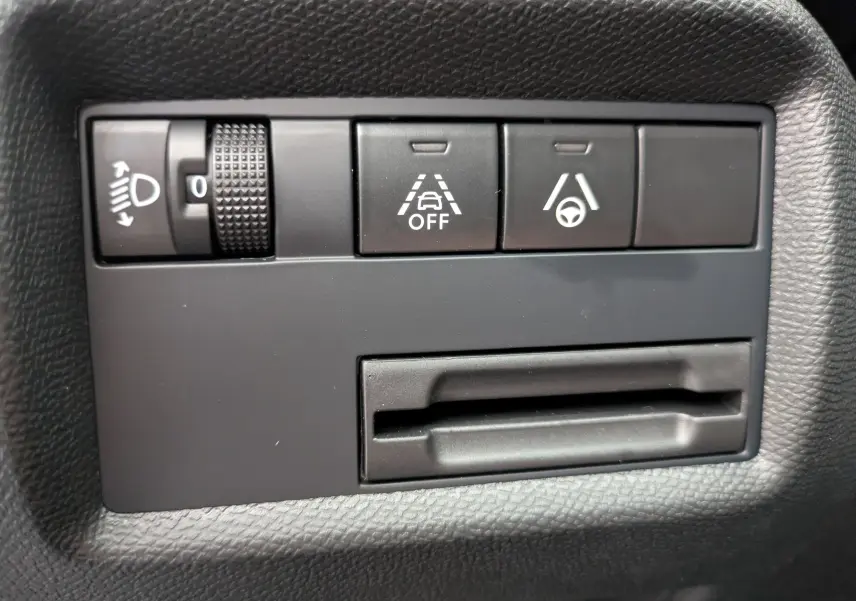 Gros plan sur les commandes de réglage des phares et d’aide à la conduite dans un Citroën C5 Aircross hybride gris platinium.