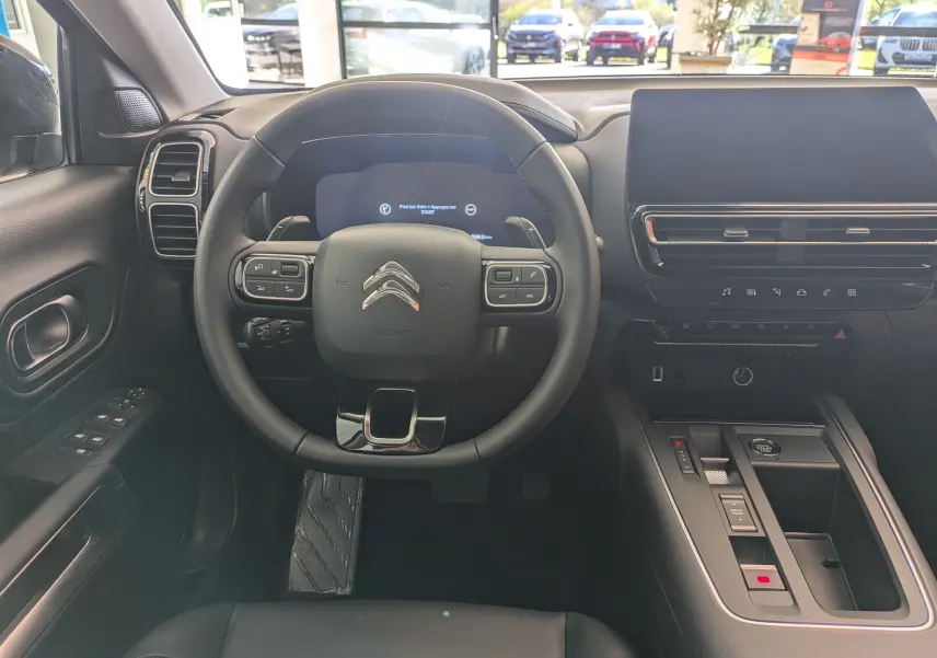 Vue intérieure centrée sur le volant et le tableau de bord du Citroën C5 Aircross hybride, ambiance noire moderne et épurée.