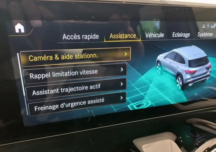 Écran tactile intérieur montrant l'assistance au stationnement avec vue 3/4 arrière d'un Mercedes GLA gris foncé.