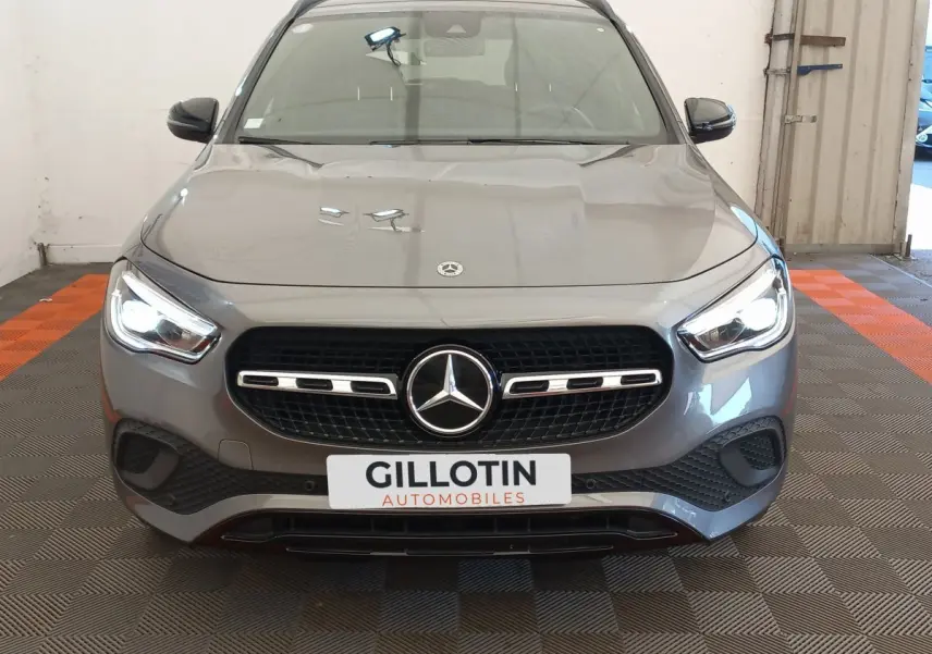 Vue frontale d'une Mercedes GLA 200 Business Line gris foncé avec phares LED allumés en intérieur showroom.