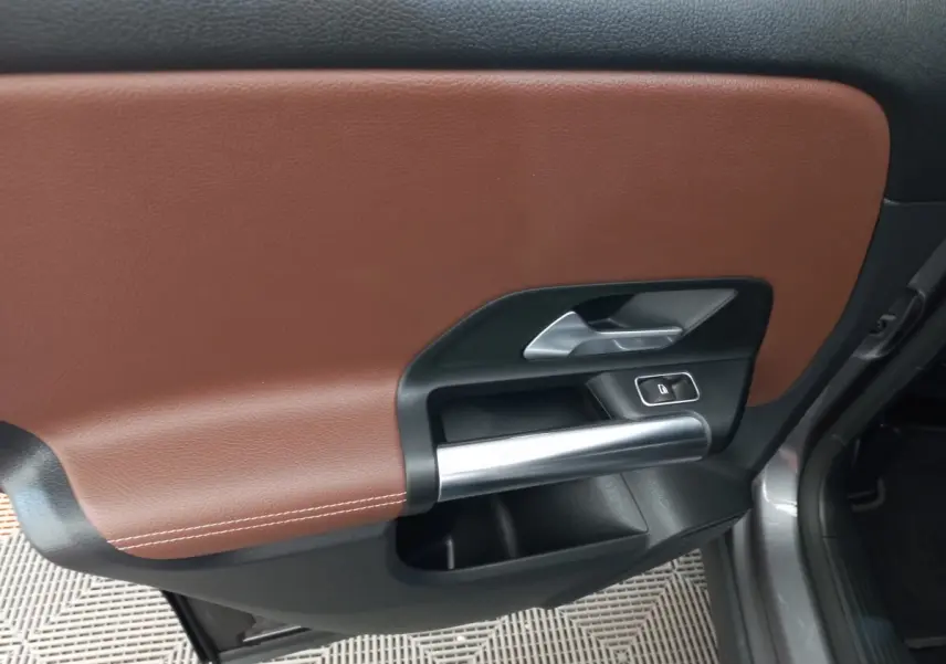 Gros plan sur la porte intérieure côté droit du Mercedes GLA gris foncé, avec garniture cuir marron et poignée argentée.