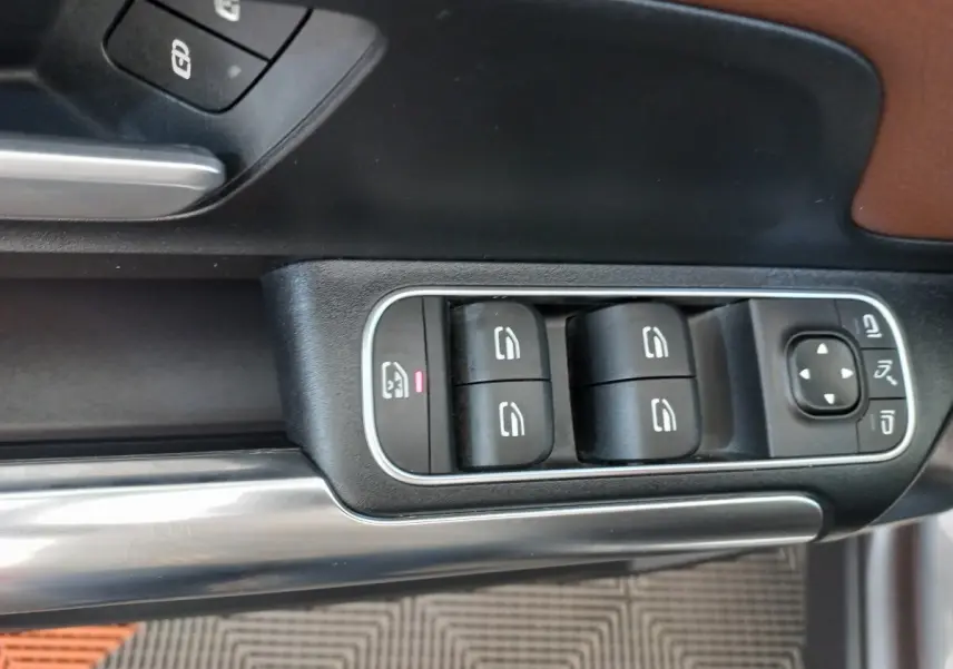 Gros plan sur les commandes de lève-vitres et rétroviseurs côté conducteur d’une Mercedes GLA 200 gris foncé.