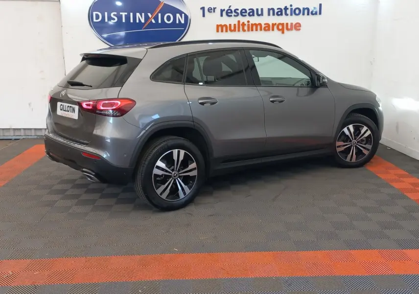 Vue 3/4 arrière droite d’un Mercedes GLA 200 Business Line gris foncé avec jantes alliage et feux LED allumés en intérieur showroom.