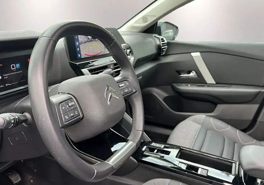 Vue intérieure côté conducteur de la Citroën C4 2024, volant cuir noir et écran tactile affichant la caméra de recul.