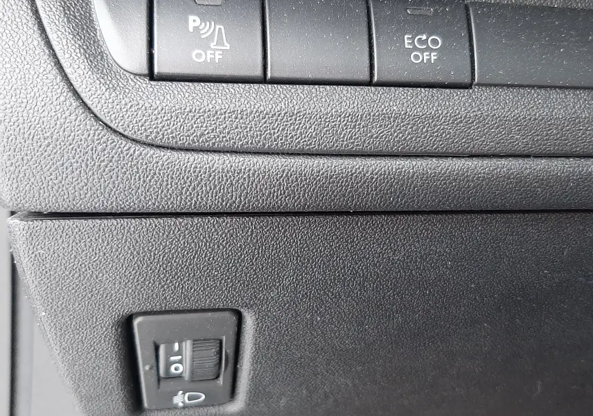 Gros plan sur les boutons de commande du tableau de bord noir du Peugeot 2008 blanc, avec fonction ECO et capteurs désactivés.