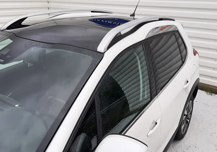Vue 3/4 avant droit du Peugeot 2008 blanc avec toit panoramique noir et barres de toit argentées.