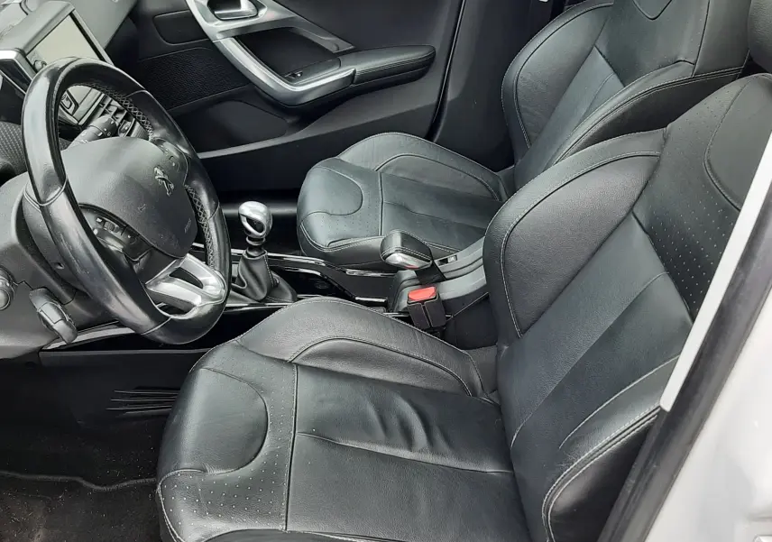 Vue intérieure côté conducteur du Peugeot 2008 blanc de 2017, sièges en cuir noir et volant multifonction.