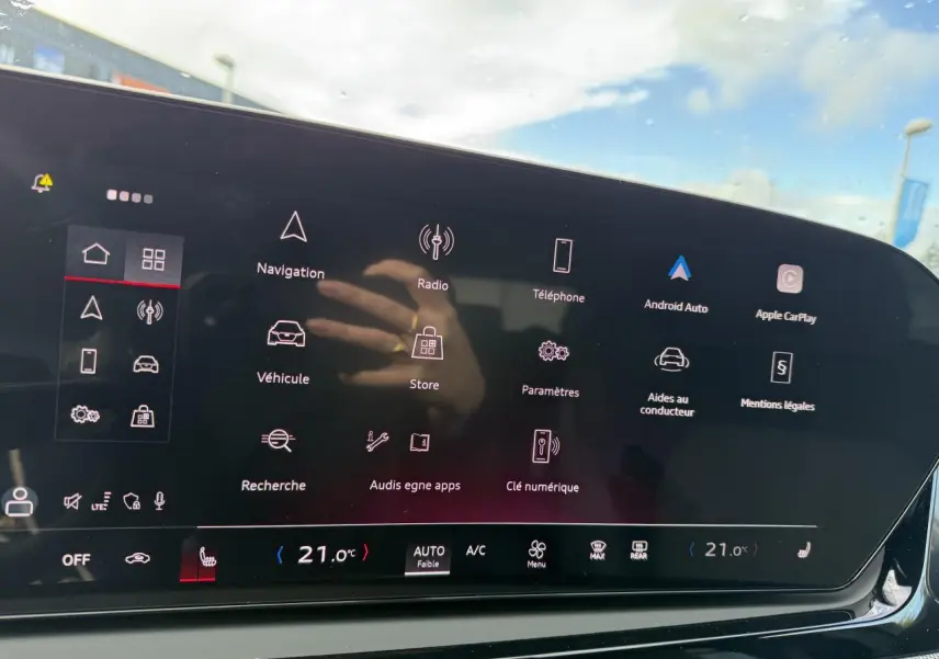 Écran tactile central de l'Audi A5 2025 affichant le menu principal avec options connectées et climatisation à 21°C.