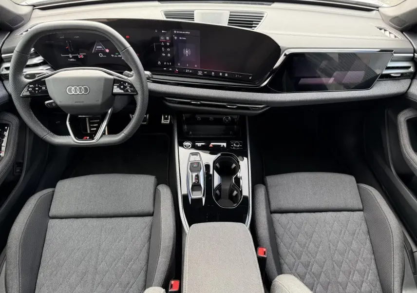 Vue intérieure de l'Audi A5 2025 montrant le tableau de bord numérique et les sièges tissu gris avec console centrale noire brillante.