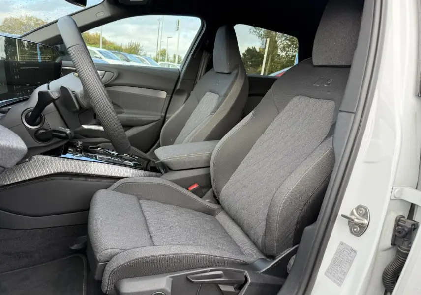 Vue intérieure côté conducteur de l'Audi A5 blanc glacier, sièges tissu gris avec logo S embossé sur appuie-tête.