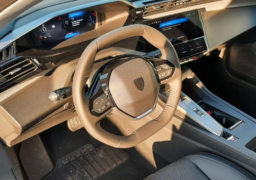 Intérieur Peugeot 308 2025 vue du poste de conduite, volant compact et tableau de bord numérique moderne noir.