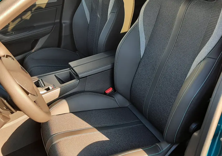 Vue intérieure côté conducteur de la Peugeot 308 2025, sièges noirs avec surpiqûres vertes et volant marron visible.