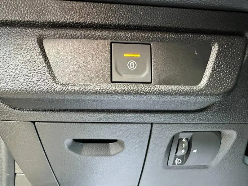 Bouton de verrouillage centralisé allumé et réglage des phares sur tableau de bord noir d'une Dacia Sandero blanche.