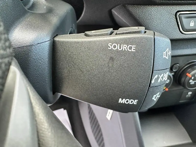 Gros plan sur la commande audio au volant côté gauche dans l'habitacle d'une Dacia Sandero blanche 2025.