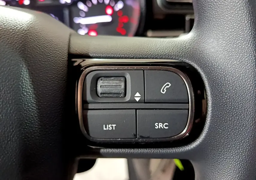 Gros plan sur les commandes du volant noir de la Citroën C3 PureTech 83 Shine 2023, boutons LIST et SRC visibles.