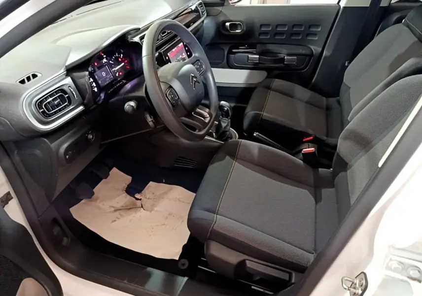 Intérieur côté conducteur d'une Citroën C3 blanche 2023, volant multifonctions, tableau de bord digital et sièges tissu noirs.