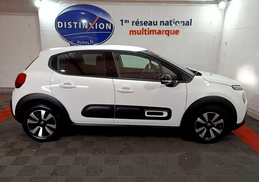 Profil côté droit d'une Citroën C3 blanche 2023 avec protections noires et jantes bicolores en intérieur showroom.