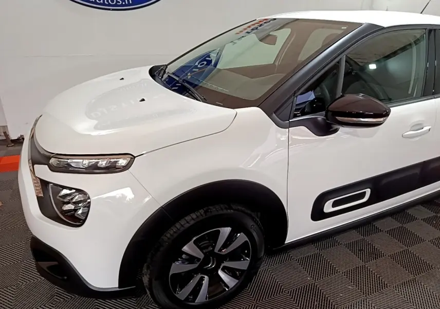 Vue 3/4 avant droit d'une Citroën C3 blanche avec rétroviseurs noirs et protections latérales caractéristiques.