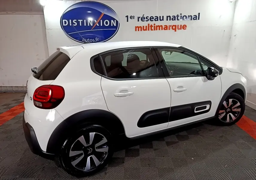 Profil côté droit d'une Citroën C3 blanche 2023 avec protections noires et jantes bicolores en intérieur showroom.