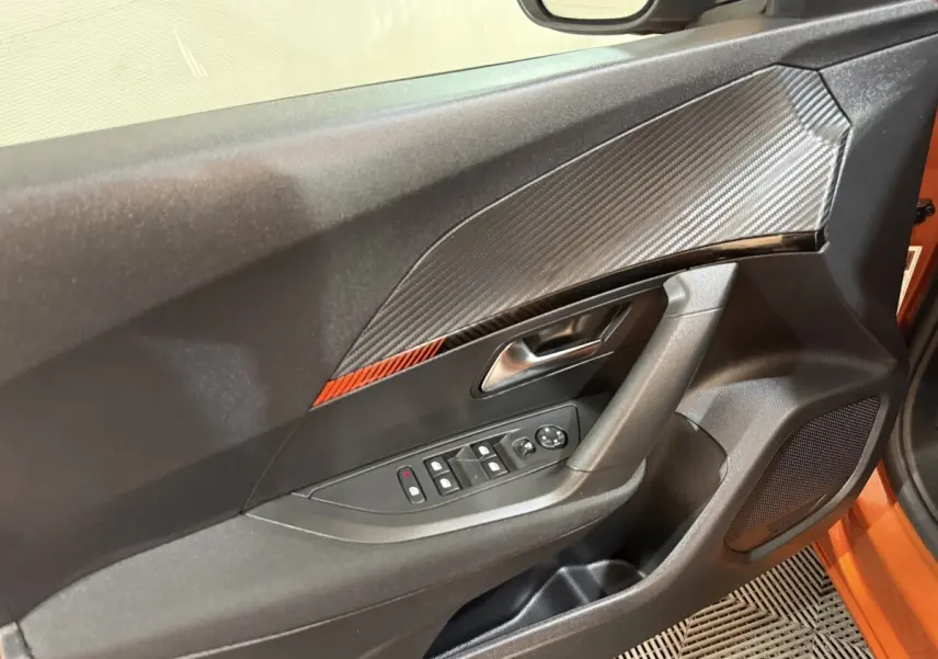 Détail de la porte avant gauche du Peugeot 2008 orange 2022 avec insert effet carbone et commandes électriques.