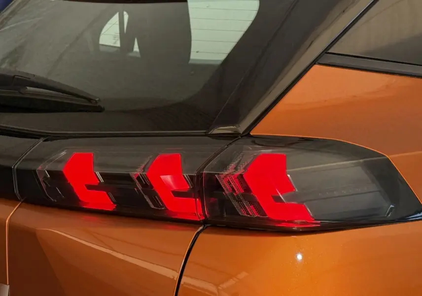 Gros plan sur le feu arrière droit rouge d’un Peugeot 2008 orange, soulignant la ligne anguleuse de la carrosserie.
