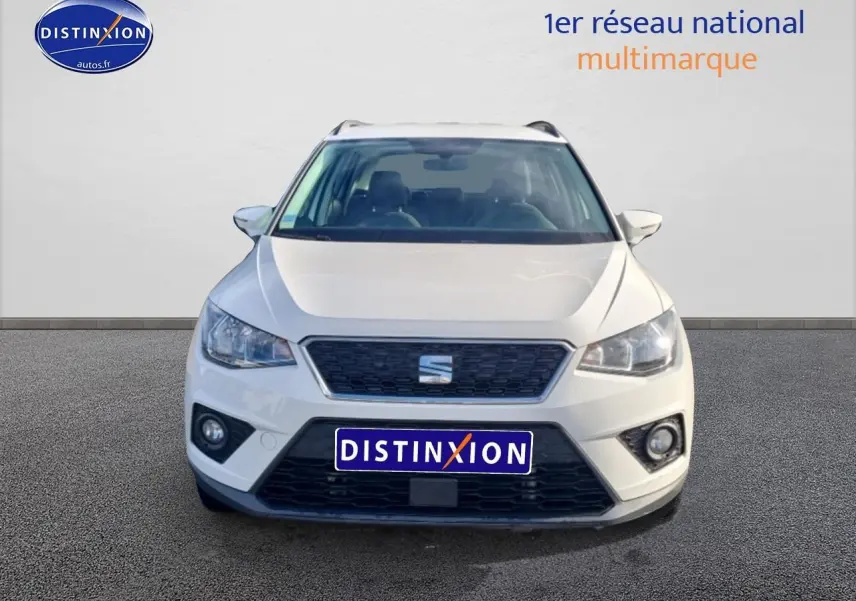 Vue frontale d'un SEAT Arona blanc 2019 avec calandre noire et phares halogènes allumés.