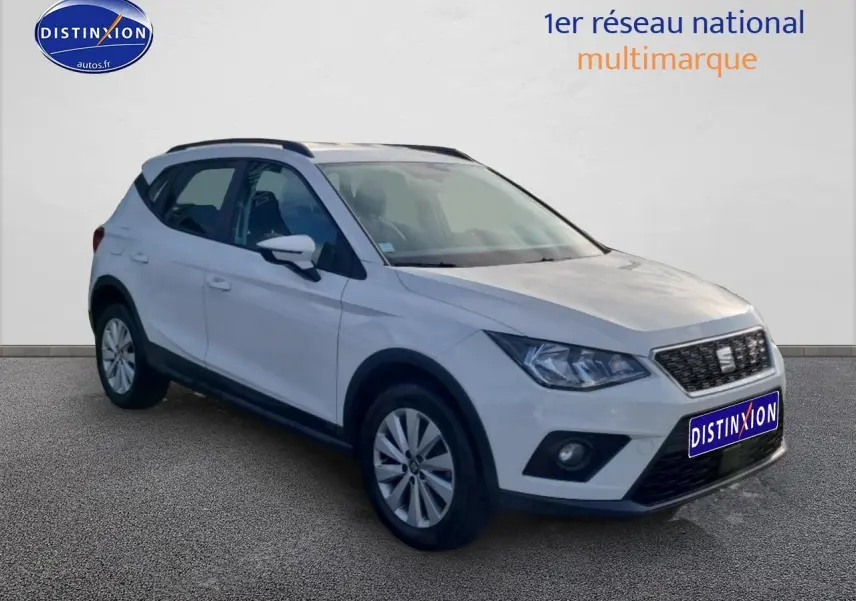 SEAT Arona blanc en vue 3/4 avant droit, avec barres de toit et jantes alliage visibles.