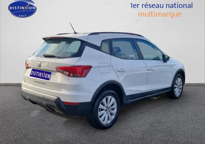 Vue 3/4 arrière droite d'un SEAT Arona blanc avec barres de toit et jantes alu.