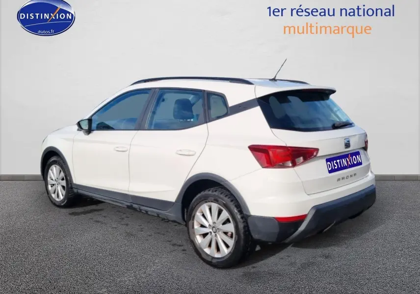 SEAT Arona blanc vue 3/4 arrière droit, avec barres de toit et jantes alliage visibles.