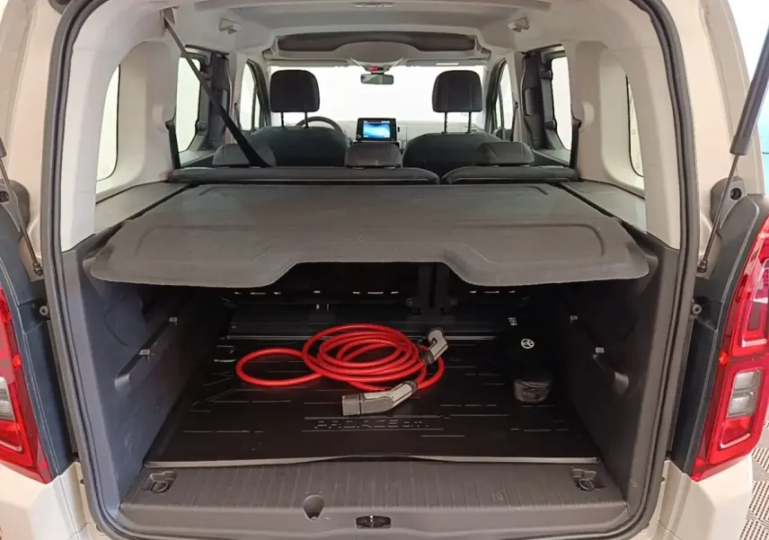 Vue arrière ouverte du Toyota Proace City Verso gris clair montrant le coffre avec câble de charge électrique rouge.