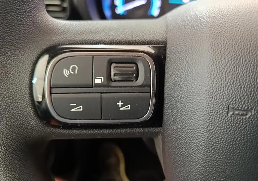 Gros plan sur les commandes gauche du volant noir du Toyota Proace City Verso électrique, avec tableau de bord flou en arrière-plan.