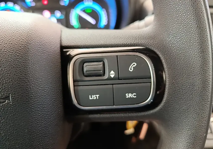 Gros plan sur les commandes gauche du volant noir du Toyota Proace City Verso électrique, avec tableau de bord lumineux en arrière-plan.